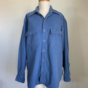 May include: A blue button-down shirt with two chest pockets. The long-sleeved shirt is displayed on a mannequin. The shirt has a collar and button closures down the front and on the cuffs.
