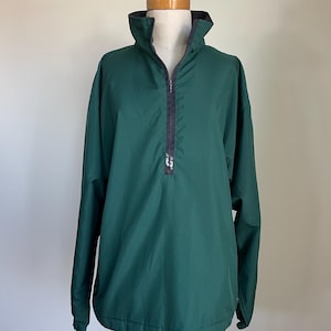 May include: A dark green pullover jacket with a high collar and a black zipper. The jacket has long sleeves and is displayed on a mannequin. The collar has a black lining.