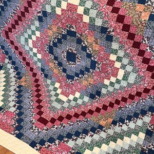 Może przedstawiać: Kołdra z patchworkowym wzorem w różnych kolorach i wzorach, w tym czerwonym, niebieskim, zielonym i kremowym. Kołdra składa się z kwadratów i prostokątów, a wzór jest symetryczny.