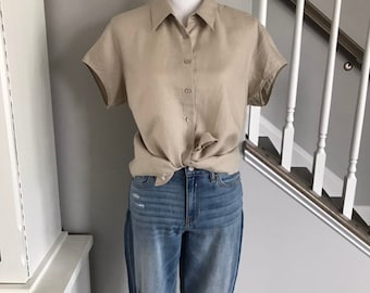 May include: A beige short-sleeved button-down shirt knotted at the waist, paired with blue denim jeans. The jeans have a relaxed fit and distressed details. The outfit is displayed on a mannequin against a neutral gray background.