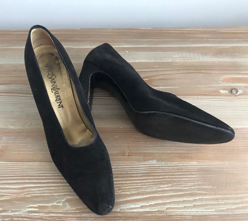 Peut inclure: Une paire de talons hauts en daim noir &agrave; bout pointu. Les talons mesurent environ 7,5 cm de haut et les chaussures sont &eacute;tiquet&eacute;es "Yves Saint Laurent".
