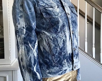May include: A light blue denim jacket with a white and blue tie-dye pattern. The jacket has a button-up front and long sleeves.