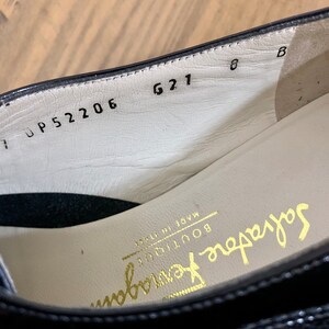 Pu&ograve; includere: Primo piano dell'interno di una scarpa in pelle nera con il testo "Salvatore Ferragamo Boutique Made in Italy" e i numeri "UP 52206 621 8 B" stampati sulla soletta.