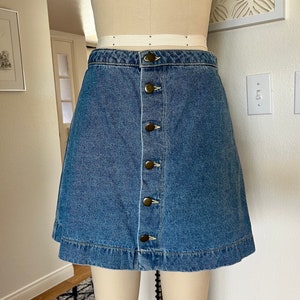 May include: A denim skirt with a button-up front and a classic A-line silhouette. The skirt is a medium blue wash and has a raw hem.