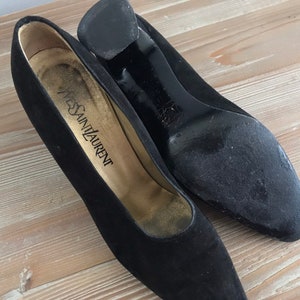 Peut inclure: Une paire de chaussures &agrave; talons en daim noir avec bout pointu. Les chaussures portent une &eacute;tiquette "Yves Saint Laurent".