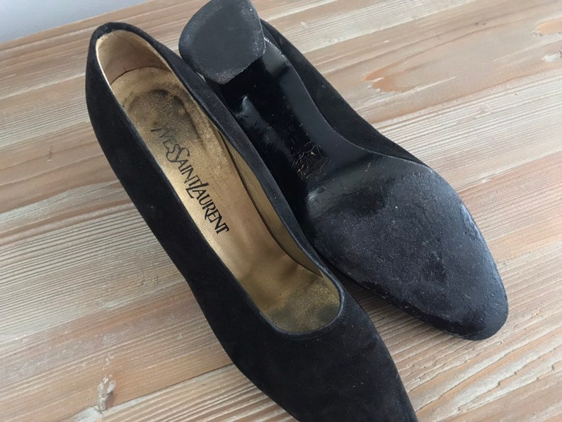 Peut inclure: Une paire de chaussures &agrave; talons en daim noir avec bout pointu. Les chaussures portent une &eacute;tiquette "Yves Saint Laurent".