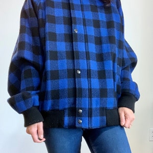 Può includere: Una giacca bomber blu e nera a quadri con chiusura a pressione e polsini e cintura a costine.