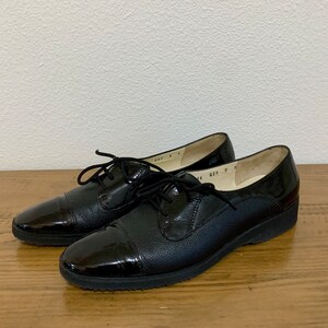 Pu&ograve; includere: Un paio di scarpe stringate in pelle nera con punta a cap. Le scarpe hanno una suola in gomma e un tacco basso.