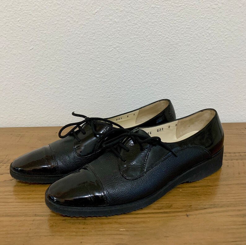 Pu&ograve; includere: Un paio di scarpe stringate in pelle nera con punta a cap. Le scarpe hanno una suola in gomma e un tacco basso.