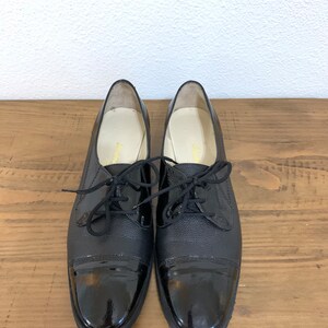 Pu&ograve; includere: Un paio di scarpe stringate in pelle nera con punta in vernice.