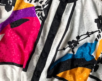 May include: A white, black, pink, purple, yellow, and blue patterned jacket with a black zipper and buttons. The jacket has a Jordana label on the collar.