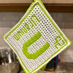 May include: A green and white crocheted pot holder with the word "HELLO" written in green on it.