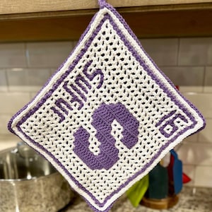 May include: Purple and white crocheted pot holder with the number "5" in the center. The pot holder has a loop for hanging.