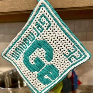 May include: A teal and white crocheted pot holder with the words "Good Eats" in teal.