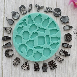 May include: A teal silicone mould with 20 different shapes of witchy and spooky designs. The mould is surrounded by 20 black resin castings of the same shapes. The text "Sissy's Creations" is visible in the image.