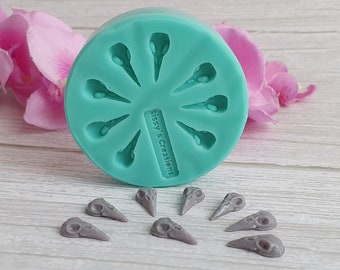 May include: A teal silicone mold with 10 bird skull shapes. There are 10 gray bird skull castings on a white wooden surface. The mold has the text "Sissy's Creations" on it.