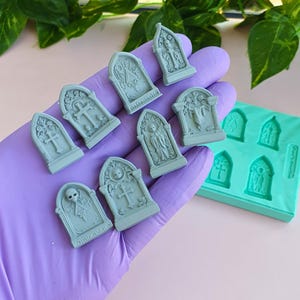 Peut inclure: Un ensemble de huit petites pièces en résine grise en forme de pierre tombale avec des sculptures détaillées de crânes, de croix et d'anges, accompagné d'un moule en silicone bleu sarcelle à six cavités pour mouler ces marqueurs.