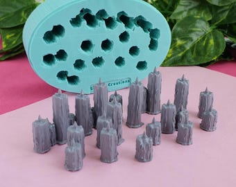 Op de afbeelding: Een lichtblauwe ovale siliconen mal met meerdere cilindrische holtes en een verzameling kleine, grijze, zuilvormige harsafgietsels. De mal is voorzien van de tekst "sili creations" in reliëf op het vooroppervlak bij de basis.