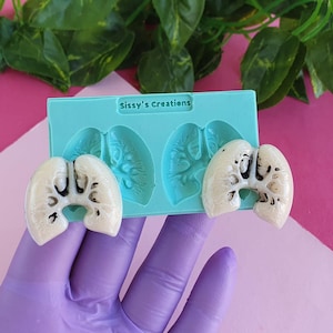 May include: A light blue silicone mould with the text "Sissy's Creations" and two lung-shaped cavities. Two off-white resin lung-shaped objects are placed next to the mould. The objects have black and white details.