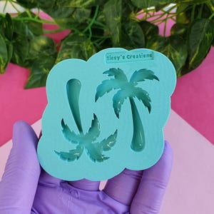 May include: A light blue silicone mould featuring two palm tree designs. The mould has the text "Sissy's Creations" at the top. The mould is held by a person wearing a purple glove.