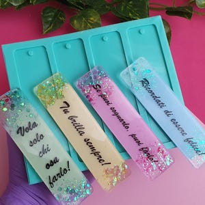 May include: Four colorful resin bookmarks with glitter and text. The bookmarks are in a teal mold. The text on the bookmarks includes phrases like "Vola solo chi osa farlo!" and "Tu brilla sempre!"