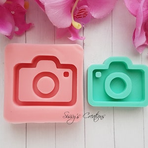 May include: Two silicone moulds for making camera-shaped objects. The larger mould is pink and the smaller mould is green.