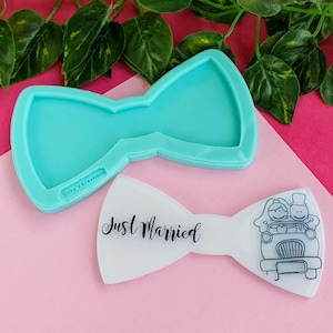 May include: A light blue bow-tie shaped mold next to a white bow-tie with the text "Just Married" and a black and white illustration of a couple in a car. The mold has the text "Sissy's Creations".