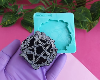 以下が含まれることがあります： 黒と白の樹脂製の五芒星が花柄で囲まれている。キャストは手袋をした手で持たれており、同じデザインのターコイズブルーのシリコンモールドの隣にある。モールドには「Sissy's Creations」という文字が印刷されている。