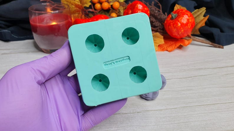 May include: A teal blue silicone mold with four round cavities. The mold is designed to create small, round objects. The mold has the text "Shay's Creations" printed on it.