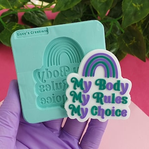 Puede incluir: Un molde de silicona para hacer manualidades de resina. El molde es azul claro y presenta un diseño de arcoíris con el texto "My Body My Rules My Choice".