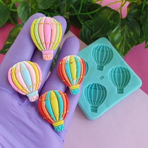 Puede incluir: Un molde de silicona con cuatro formas de globo aerostático. El molde es azul claro y los globos son de varios colores, incluyendo rosa, azul, amarillo y rojo.