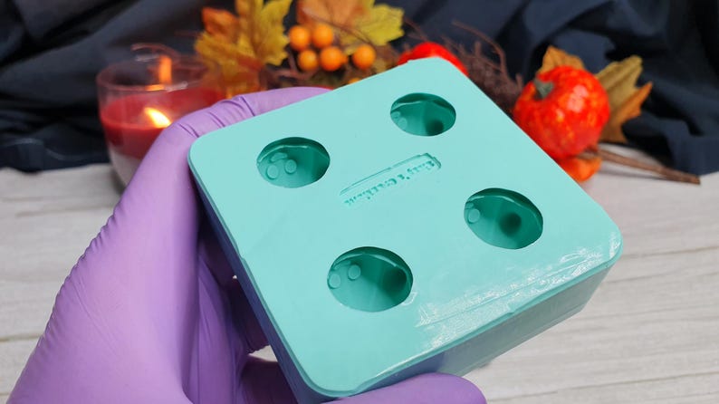 May include: A turquoise silicone mold with four round cavities. The mold is designed for making small round objects, such as candles or soap.