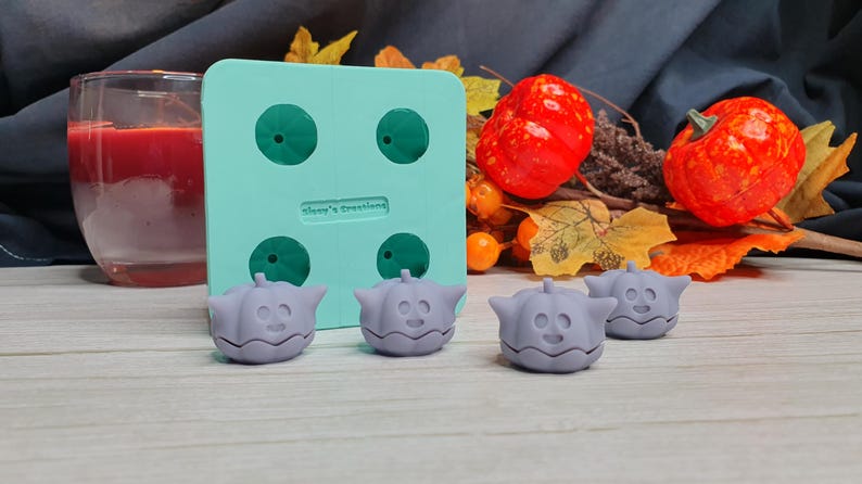 May include: A teal silicone mold with four pumpkin-shaped cavities. Four gray pumpkin-shaped silicone molds are sitting on a wooden surface. The mold is labeled "Always Creating".