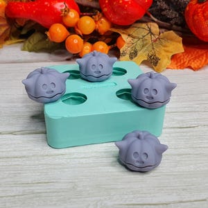 May include: A teal silicone mold with four pumpkin-shaped cavities. The mold is filled with four purple pumpkin-shaped candies.