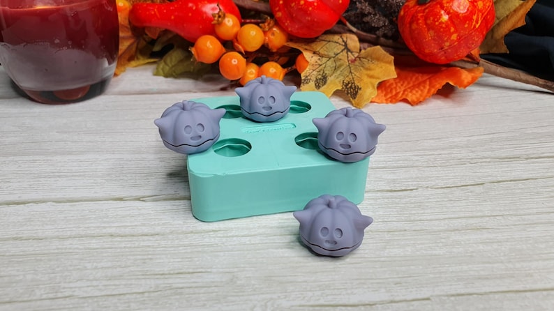 May include: A teal silicone mold with four pumpkin-shaped cavities. The mold is filled with four purple pumpkin-shaped candies.