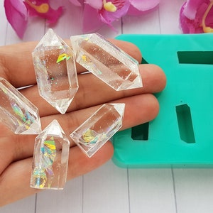 May include: Four clear, double-terminated resin crystals featuring embedded iridescent foil flakes and fine glitter, displayed alongside a rectangular teal silicone mold with four empty cavities designed for casting these crystal shapes.