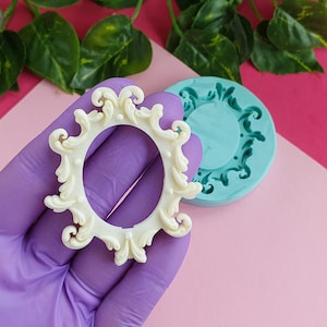 Puede incluir: Un molde de silicona blanco para hacer un marco decorativo. El molde tiene forma de círculo con un diseño detallado y ornamentado. El molde se muestra junto a un marco blanco que se ha hecho utilizando el molde.