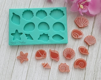 May include: A teal silicone mold with 12 different seashell and starfish shapes.  The mold is on a white wooden surface with several pink resin seashells and starfish.