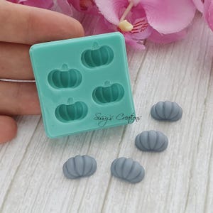 May include: A teal silicone mold with five pumpkin-shaped cavities and several gray pumpkin-shaped resin castings. The mold has the text "Sissy's Creations" in cursive. The pumpkins are a fall-themed craft supply.