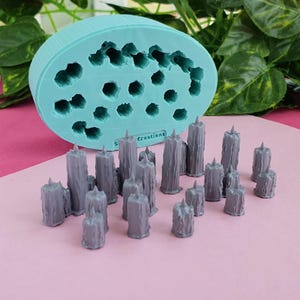 May include: A teal silicone mould with 18 cavities for making candles. The mould is next to a group of 17 grey, textured, pillar candles.