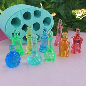 Puede incluir: Una colección de pequeñas botellas de perfume de colores, en tonos azules, verdes, amarillos, naranjas y rosas. Se ve un molde de silicona turquesa con cavidades en forma de botella. Las botellas están dispuestas sobre una superficie rosa claro.