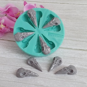 May include: A teal silicone mould with eight grey bird skull shapes, plus six detached skulls. The mould is labelled "Sissy's Creations". Pink orchids are in the background. The skulls are detailed resin castings.
