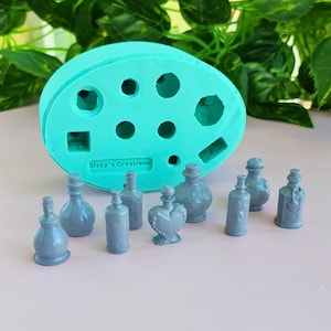 Puede incluir: Un molde de silicona azul claro con el texto Sissy's Creations en relieve en el frente, acompañado de nueve pequeñas figuras grises en miniatura con forma de botella en varios diseños, incluyendo formas de corazón y cilíndricas.