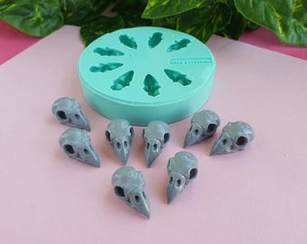 May include: A silicone mold with eight bird skull shapes, and eight gray resin bird skulls on a pink surface.