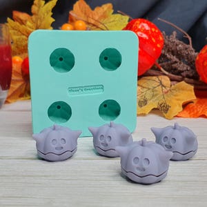 May include: Four small purple pumpkin-shaped silicone molds with a green silicone mold with four pumpkin-shaped cavities in the background.  The text "Dawn's Creations" is printed on the green mold.