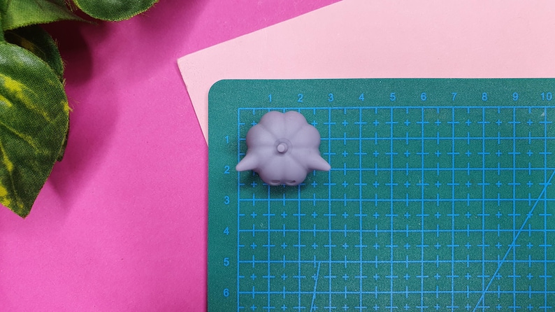 May include: A light purple, 3D printed, pumpkin-shaped object with a stem on top. The object is sitting on a green cutting mat with a grid pattern.