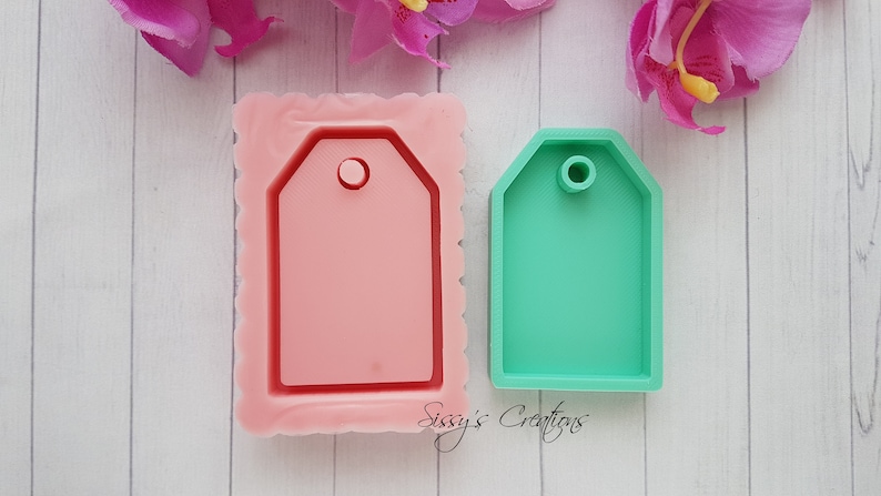Puede incluir: Dos moldes de silicona para hacer manualidades de resina. El molde de la izquierda es rosa y tiene un borde festoneado. El molde de la derecha es verde y tiene un borde liso. Ambos moldes tienen forma de etiqueta con un agujero en la parte superior.