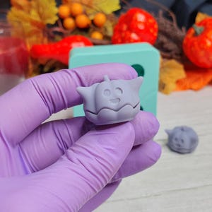 May include: A purple silicone mold with a small, light purple pumpkin-shaped mold. The pumpkin mold has a smiling face.