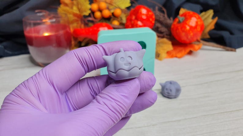 May include: A purple silicone mold with a small, light purple pumpkin-shaped mold. The pumpkin mold has a smiling face.