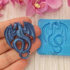 Op de afbeelding: Een blauwe siliconen mal voor het maken van een drakenvormige taarttopper of decoratie. De mal wordt getoond met een afgewerkte draak gemaakt van blauwe hars.